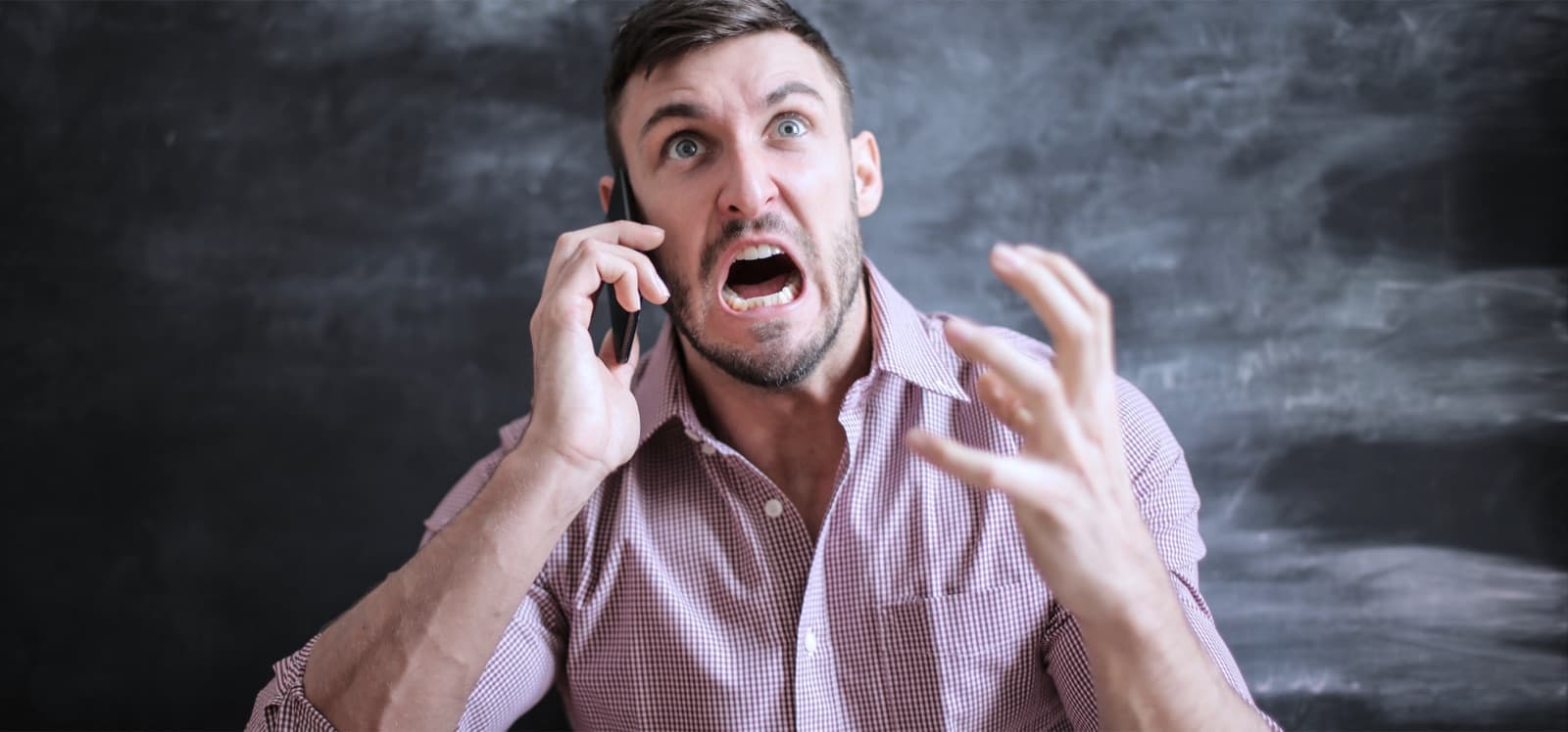 Hombre expresando enojo al hablar por teléfono frente a un pizarrón