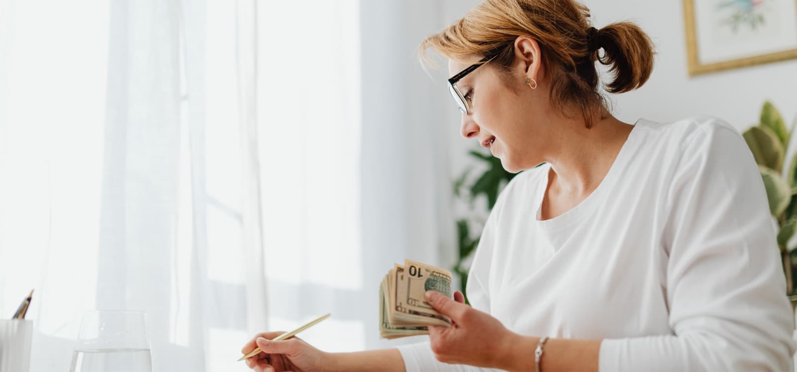 Mujer contando billetes junto a una ventana
