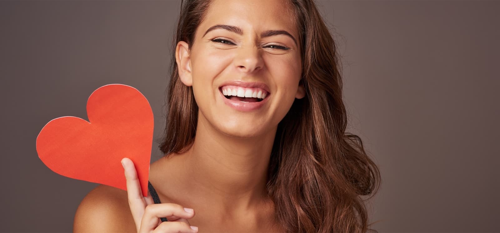 Mujer riendo sosteniendo un corazón de papel rojo