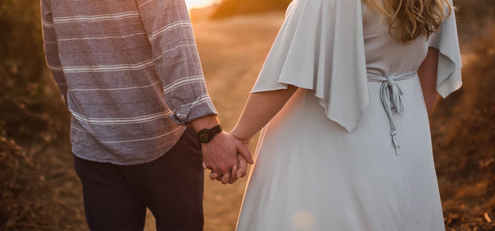 Pareja de espaldas tomados de la mano, caminando al atardecer