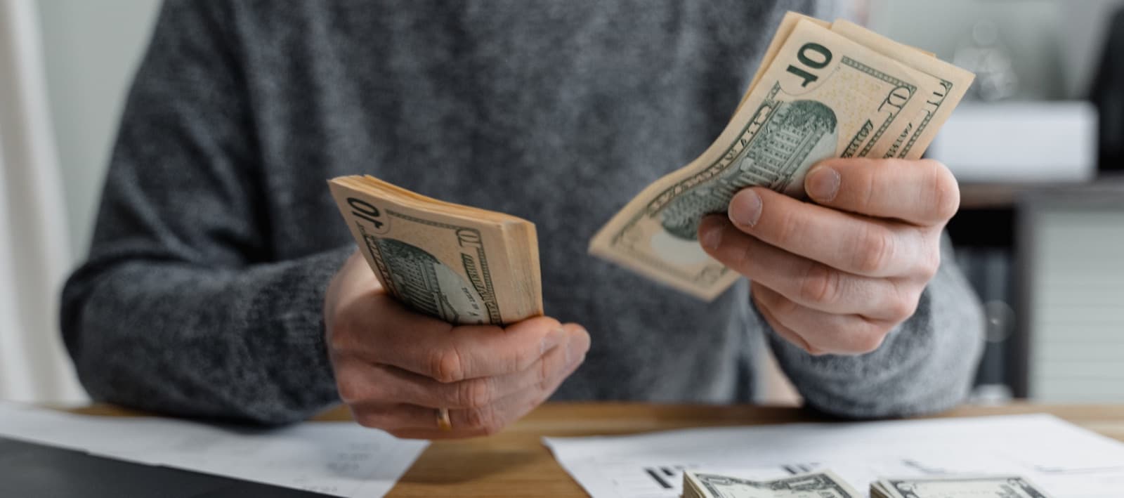 Manos contando billetes sobre un escritorio con documentos