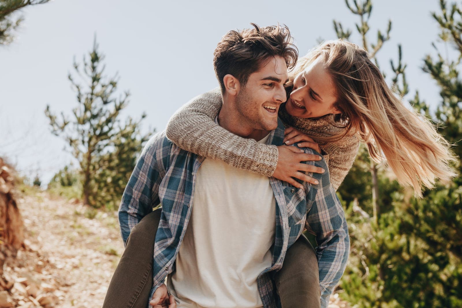 Esposo cargando a su esposa en la espalda mientras ambos sonríen al aire libre