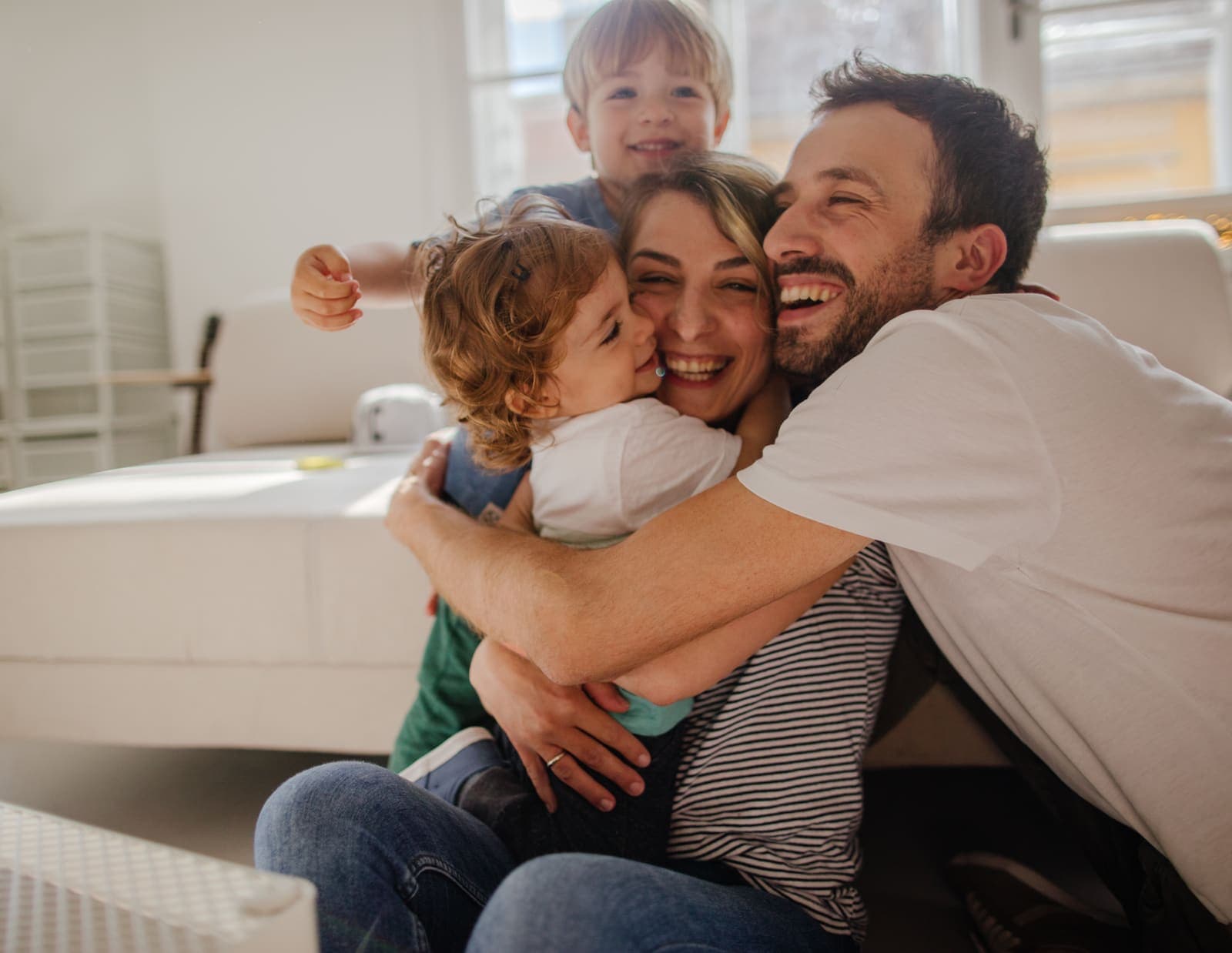 Padres abrazando a sus dos hijos pequeños en el salón de casa