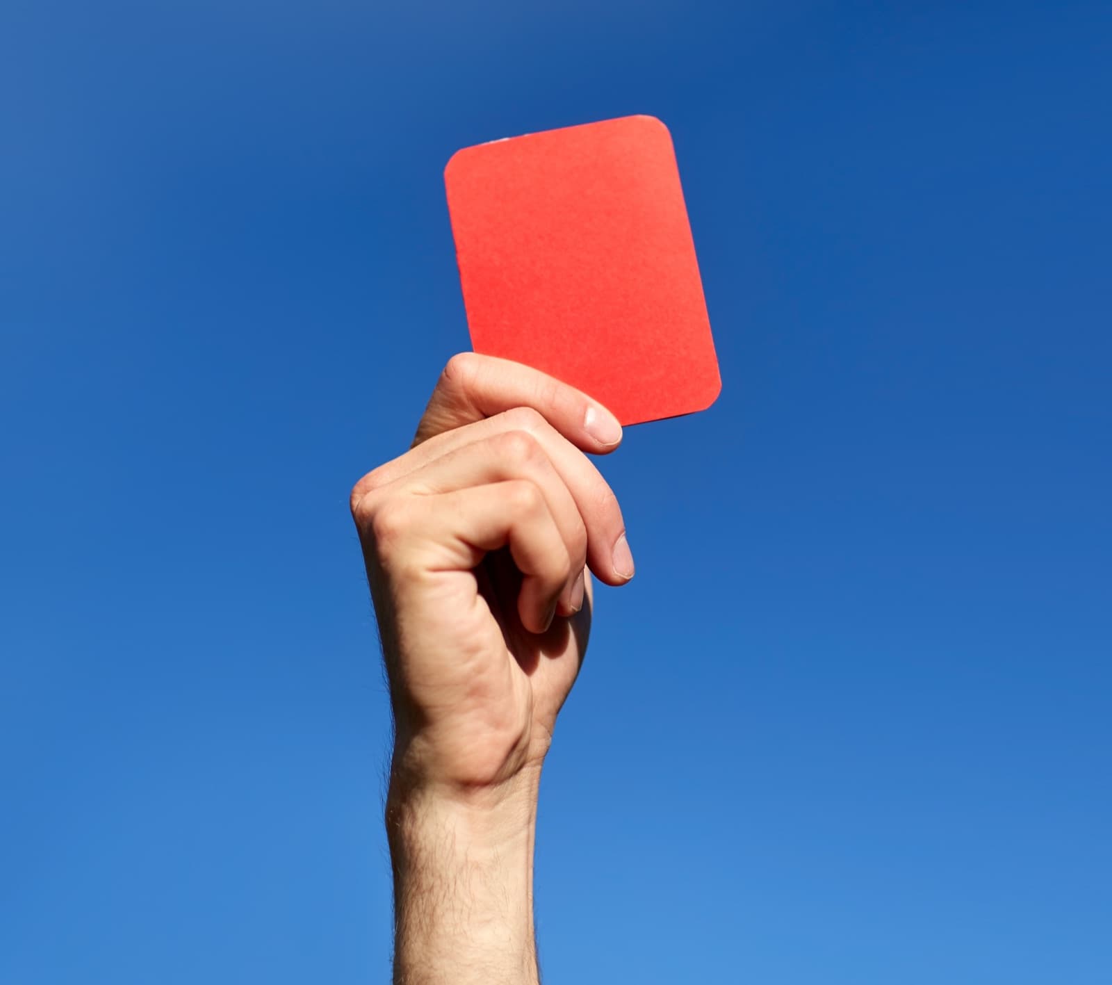 Mano sosteniendo una tarjeta roja contra un cielo azul