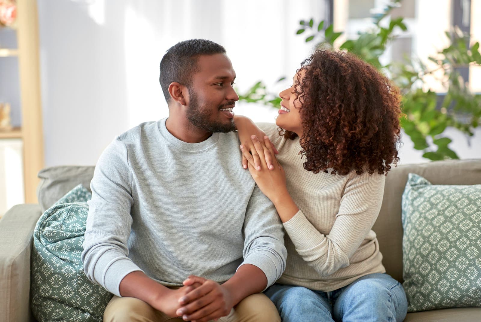 Matrimonio sentado en el sofá de su casa, mirándose y sonriendo